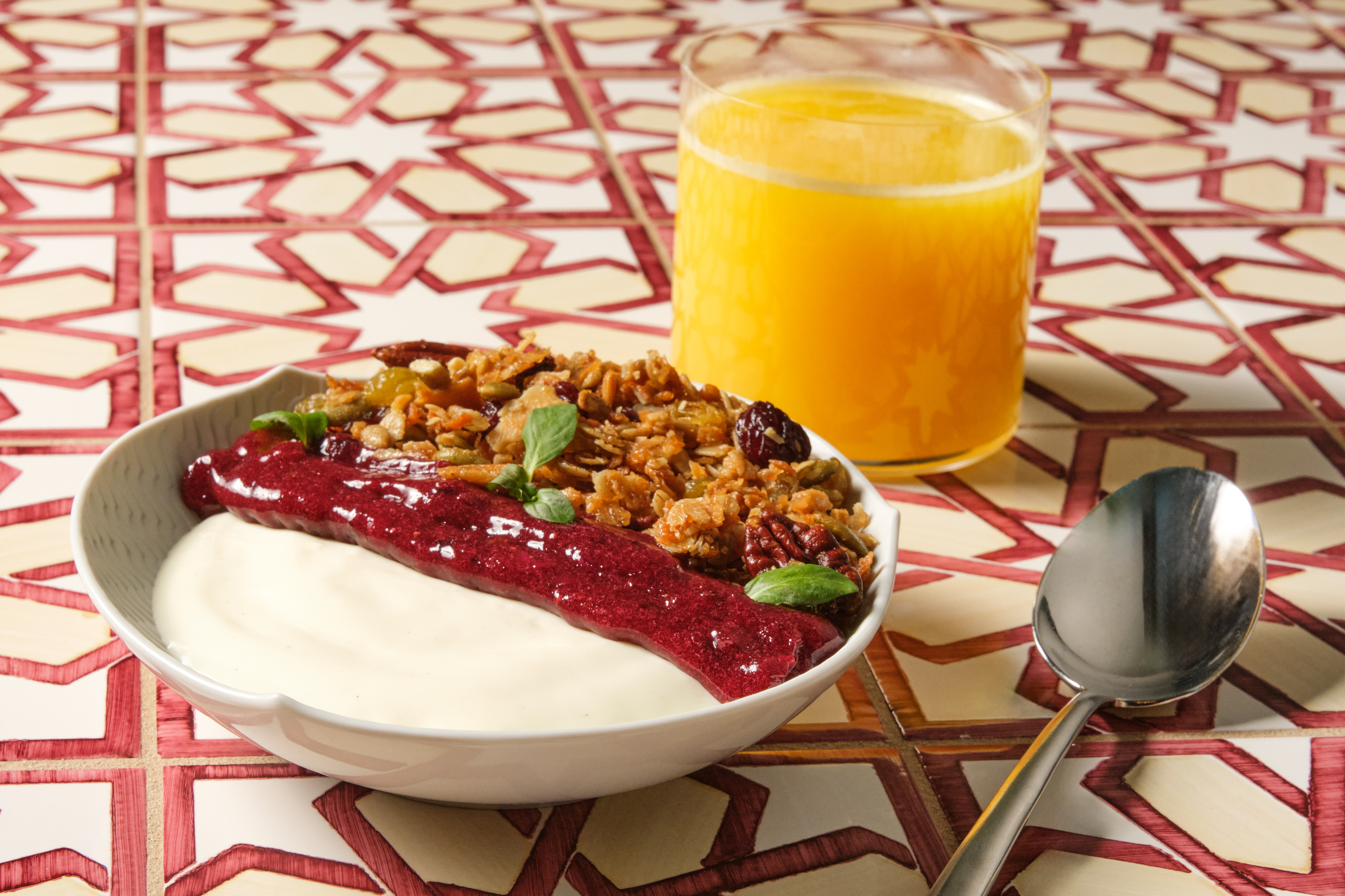 a glass of fresh squeezed orange juice next to a parfait with red berry jam and granola.