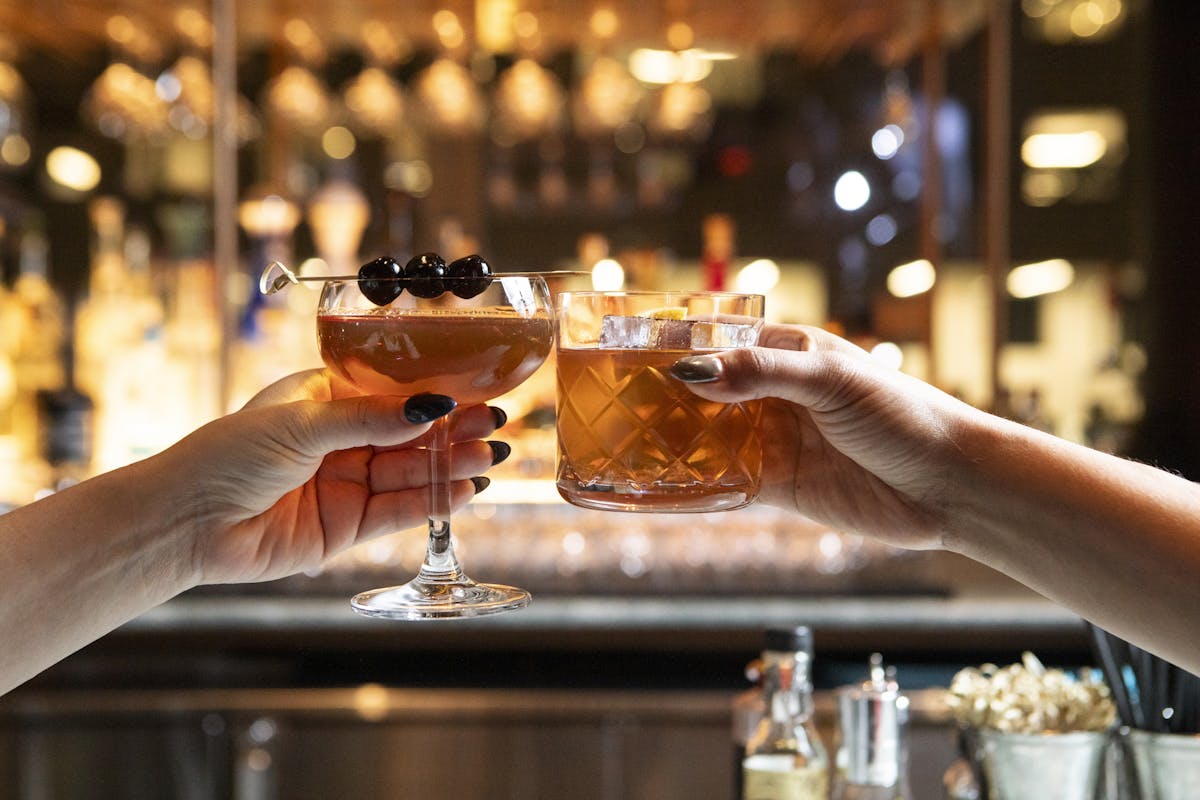 two people holding cocktails in front of a bar