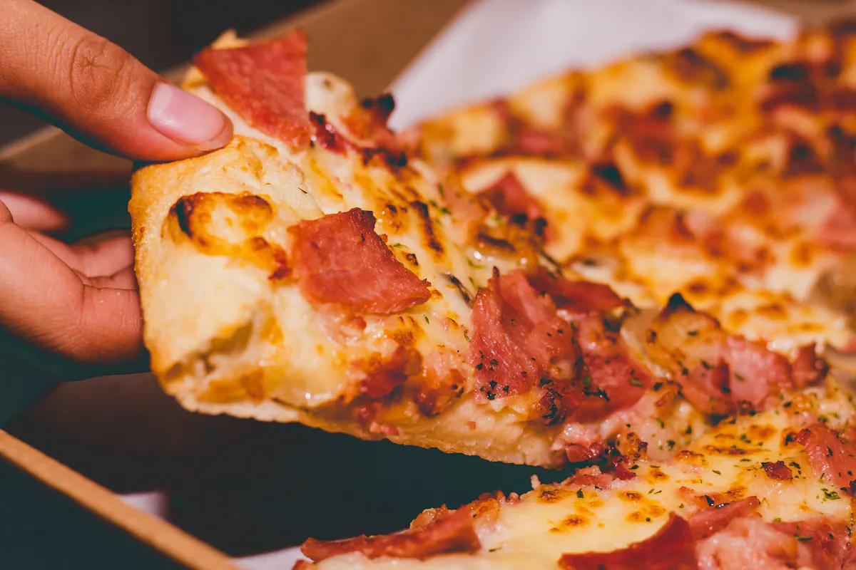 a hand holding a slice of pizza