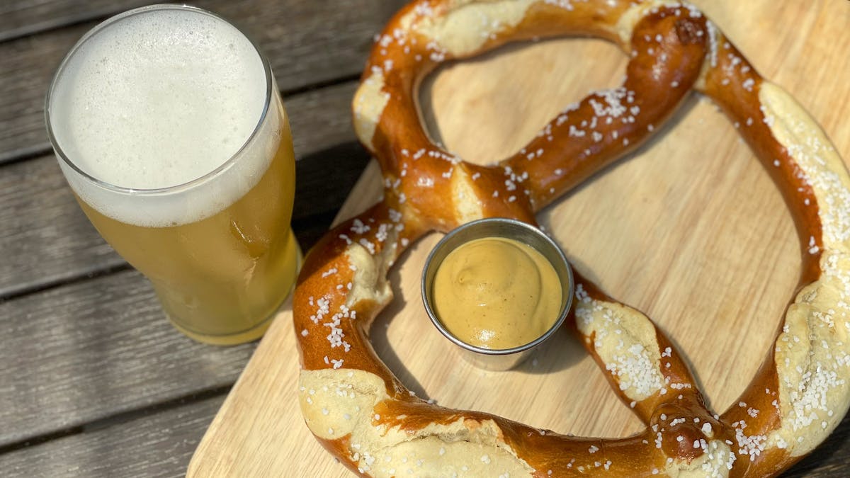 Glass of IPA beer on the left. On the right is a pretzel on a wood board.