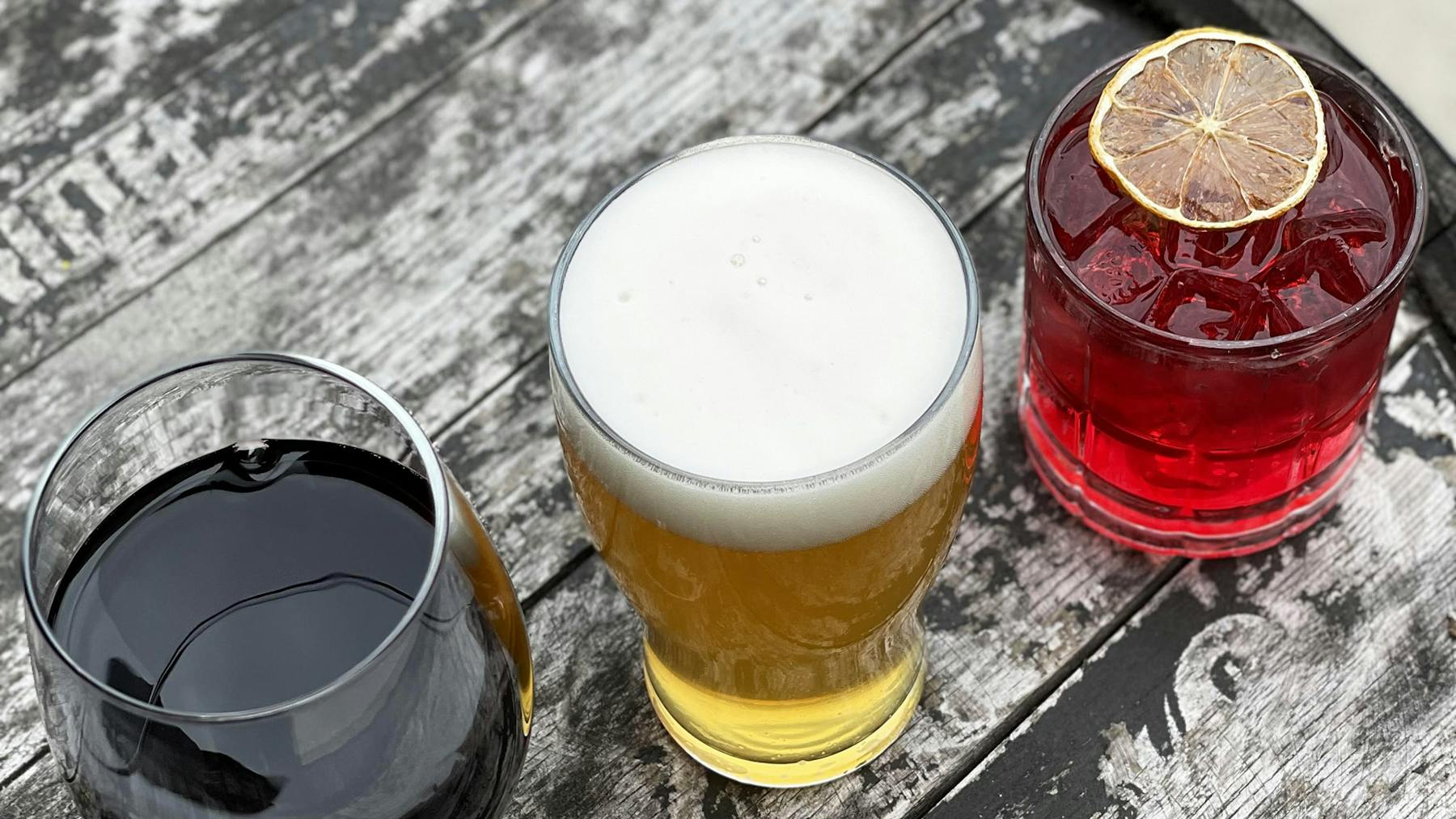 a glass of red wine, glass of beer, and a red cocktail on barrel