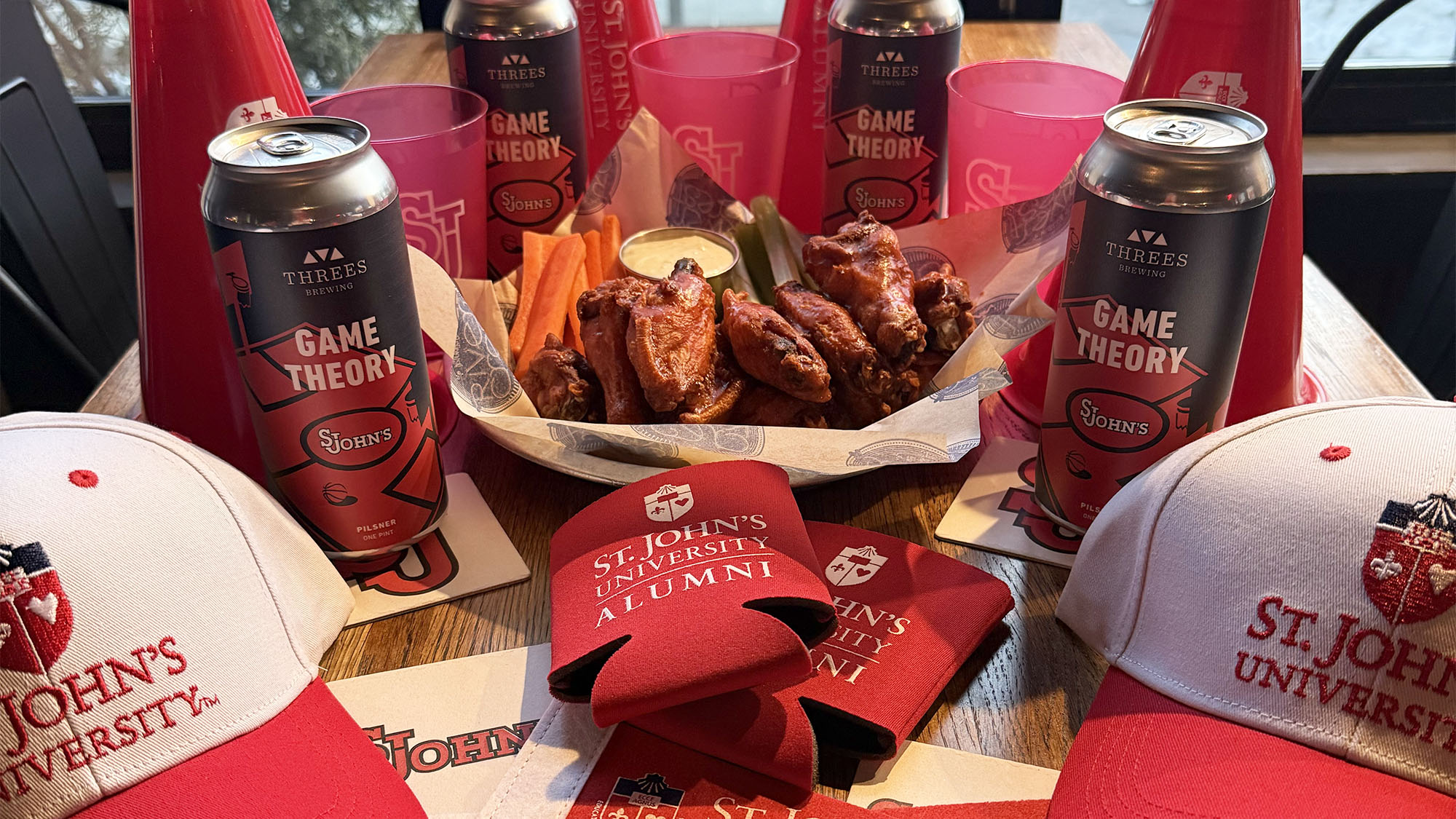 $1 wings, cans of Threes Game Theory and a lot of SJU gear on table at Rivercrest in Astoria, Queens