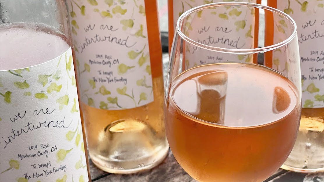 a glass of rosé and bottles of rosé in the back