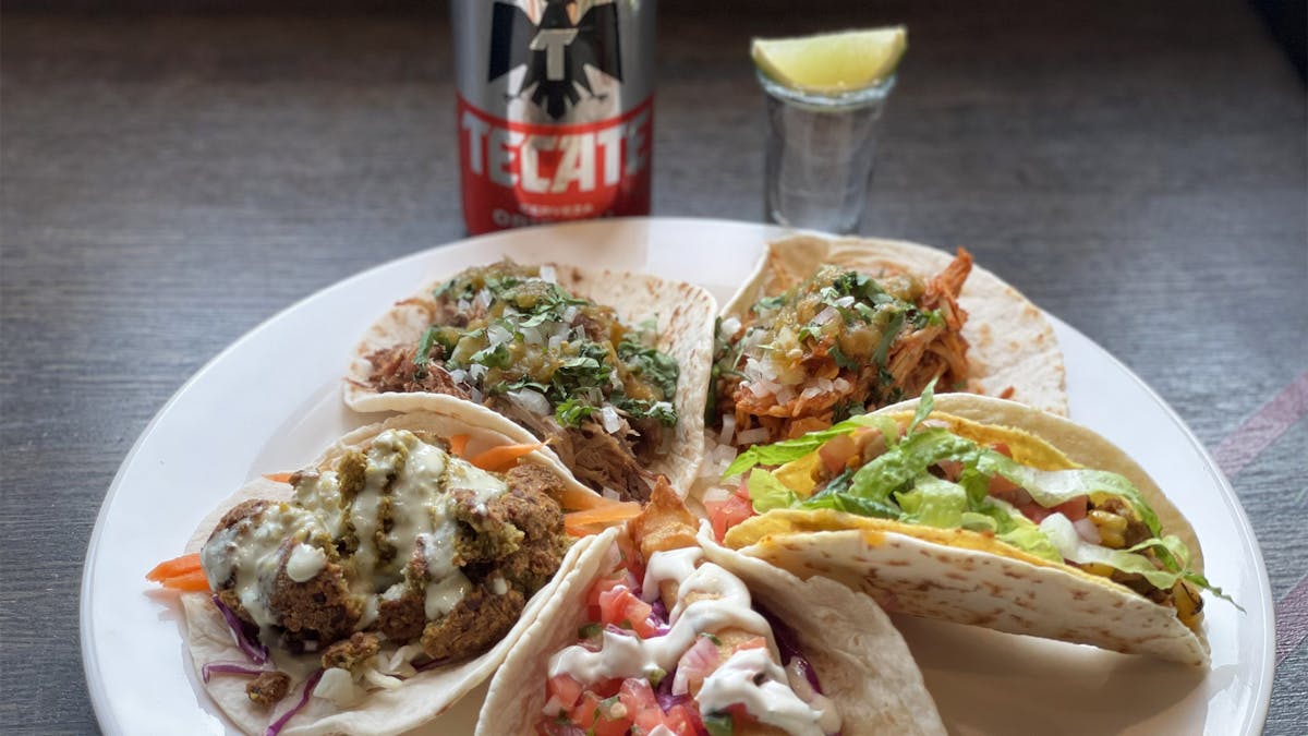 a plate of various Rivercrest tacos with a can of Tecate and tequila shot in the back