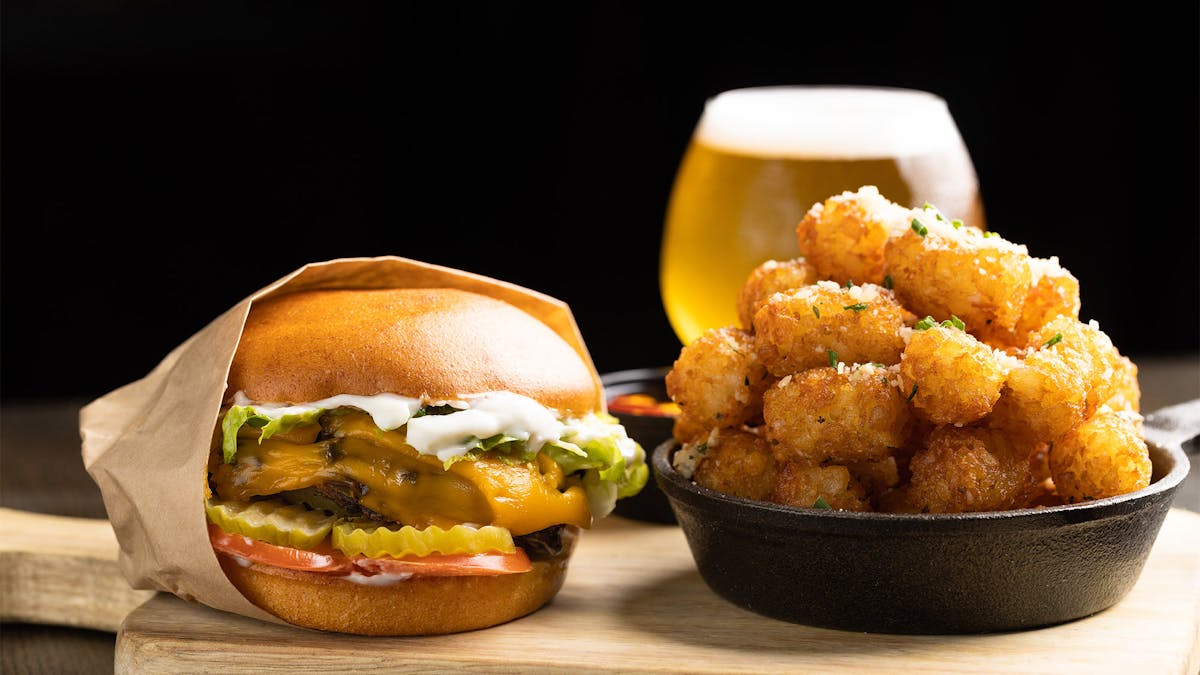 Rivercrest's Housemade Vegan Burger on a wooden board with tater tots and beer in the background