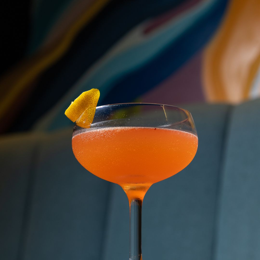 Orange cocktail in a coupe glass with a citrus garnish.