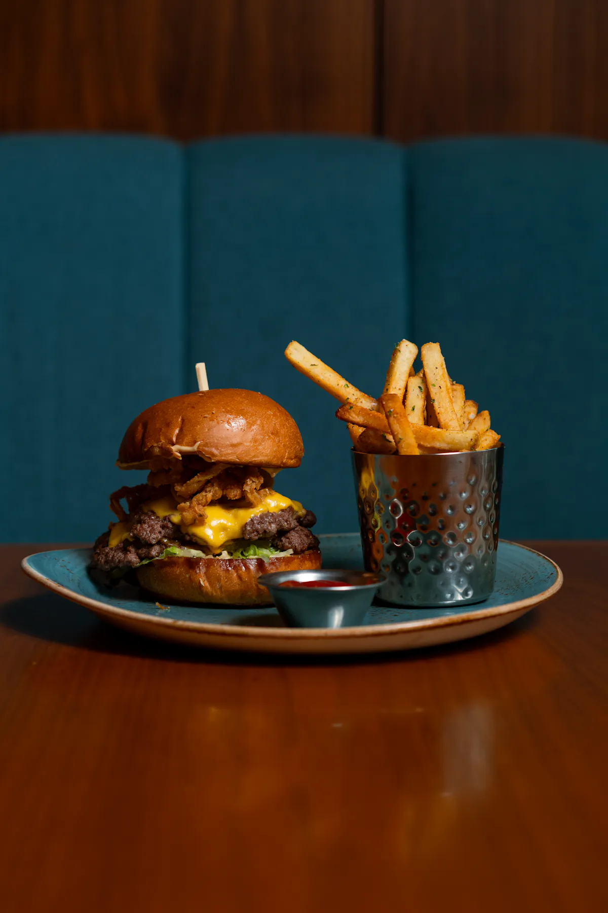 Gourmet cheeseburger with fries and dipping sauce served on a teal plate.