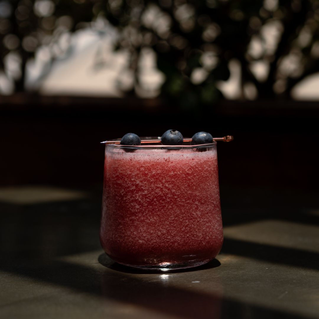Blueberry cocktail in a low glass with dark rooftop lighting.
