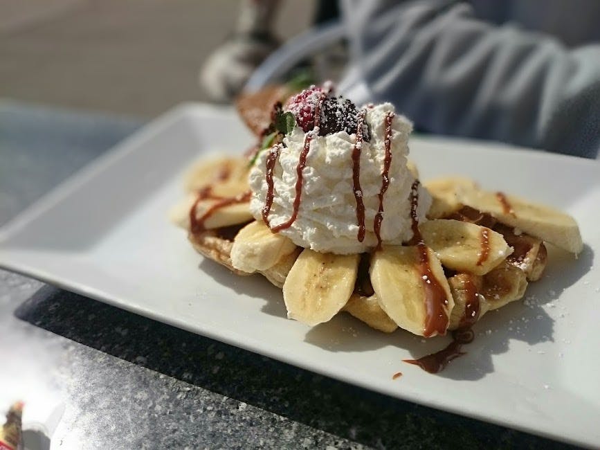 a waffle with bananas chocolate and whipped cream on a plate