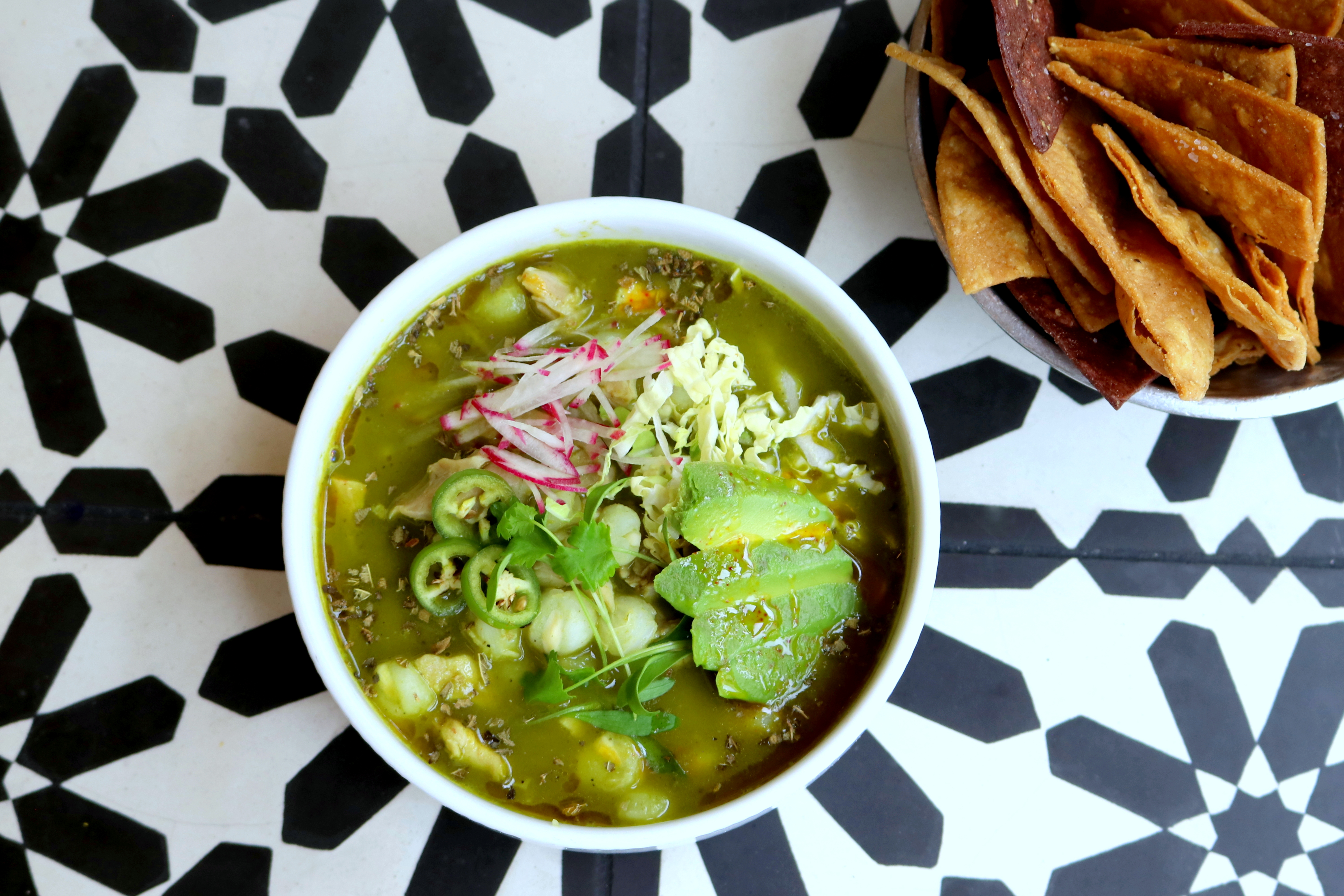 a bowl of green soup with vegetables and chips