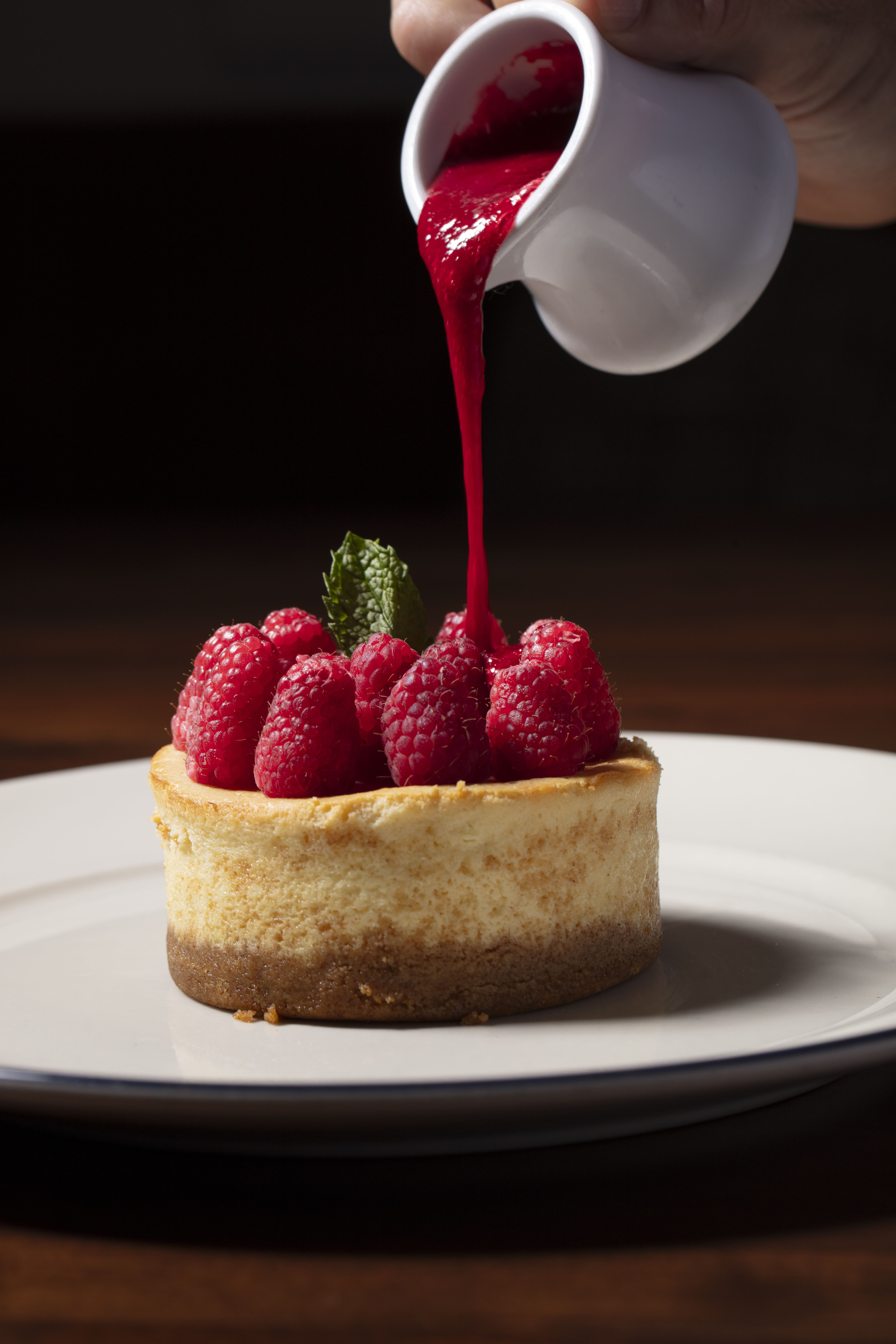 a raspberry cheesecake with raspberries and mint leaves on a white plate