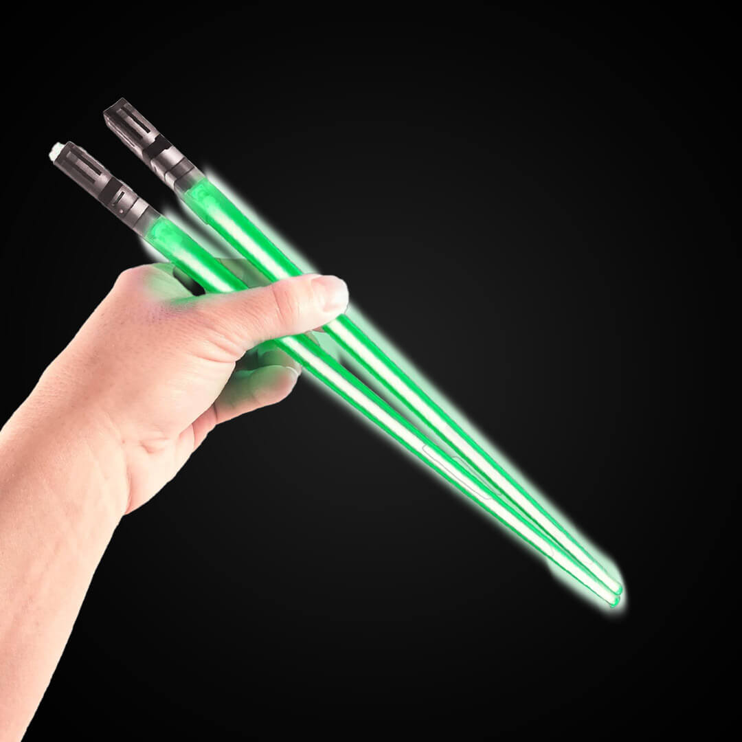 A hand holding a pair of glowing green LED chopsticks styled to look like miniature sci-fi lightsabers.