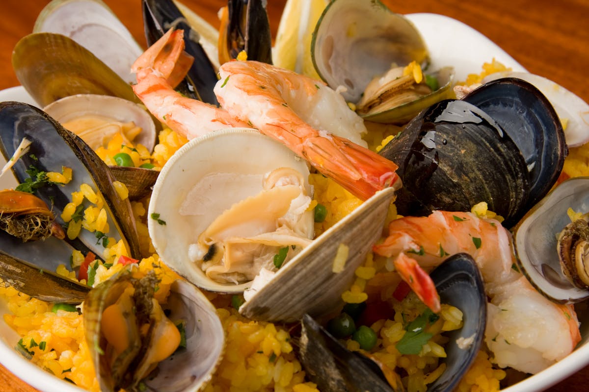 Close up of Seafood Paella Valenciana showing clams, mussels, shrmip and chicken atop arborio rice