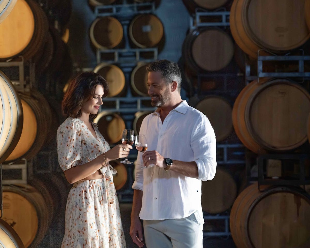Couple of people with wine glasses at South Coast Winery with wine barrels in background.