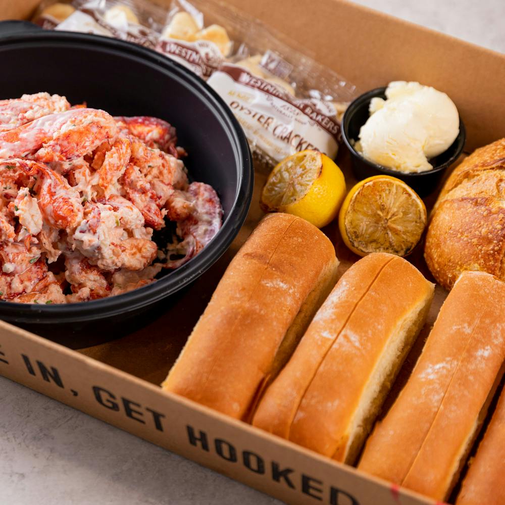 cardboard tray with lobster kit ingredients including lobster, lemons, butter, rolls and crackers