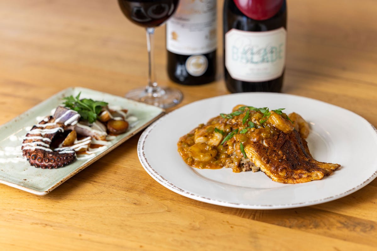 Grilled Spanish Octopus and Nawlins' Blacked Chicken beside two bottles of wine and a wine glass.