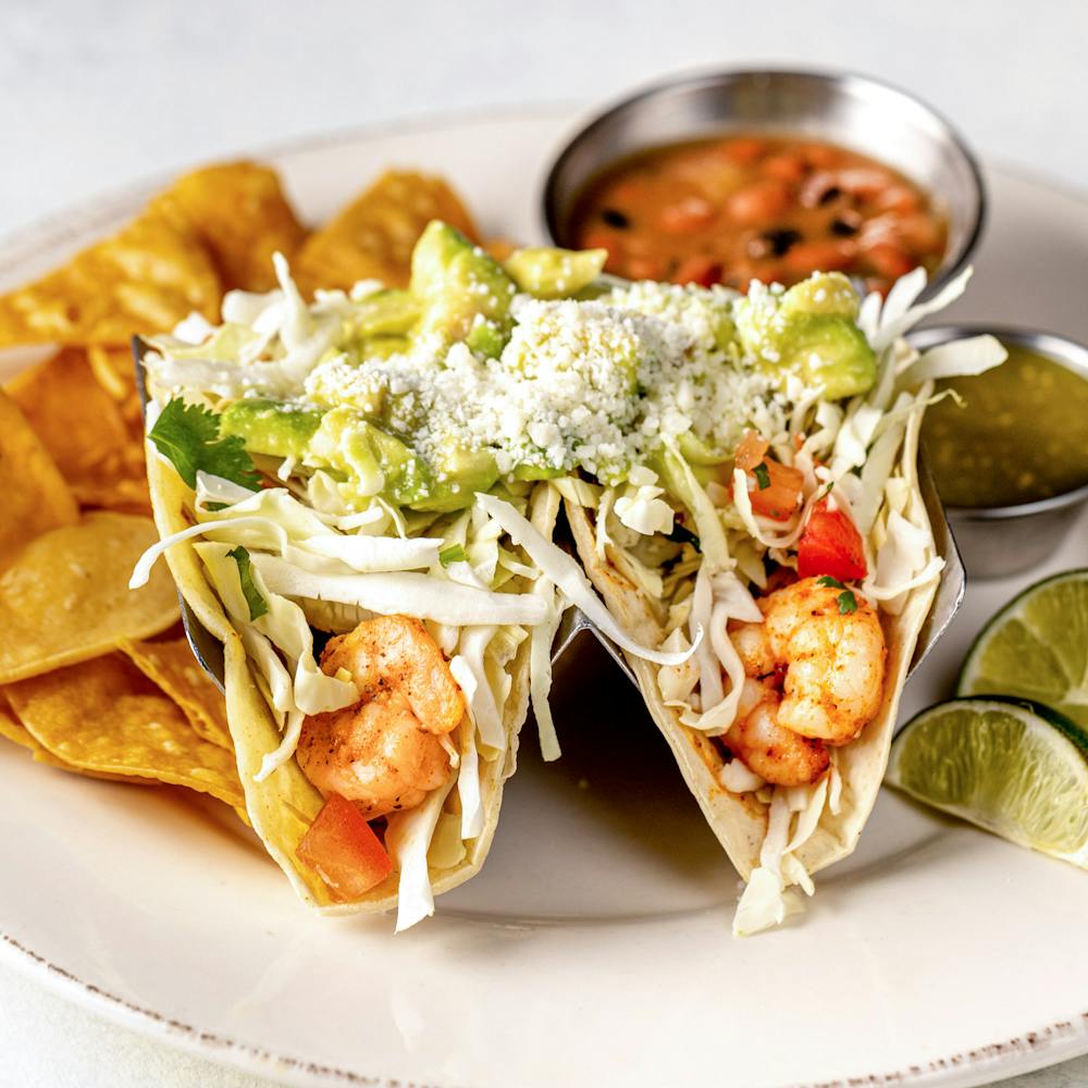 Blackened shrimp tacos with cheese, cabbage, pico de gallo, lime crema and avocado on a plate with tortilla chips. 