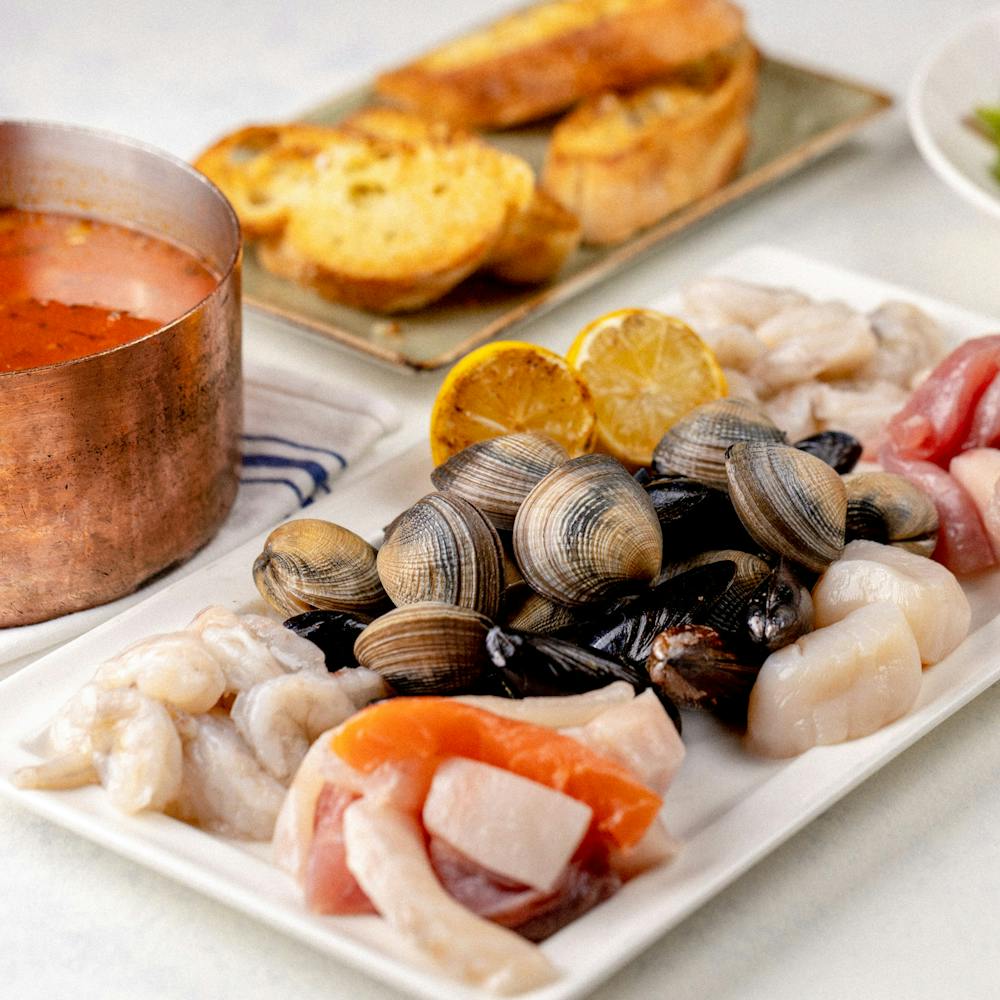 Cioppino ingredients including pot of marina and assortment of shrimp, scallops, mussels, clams, fish and crabmeat.