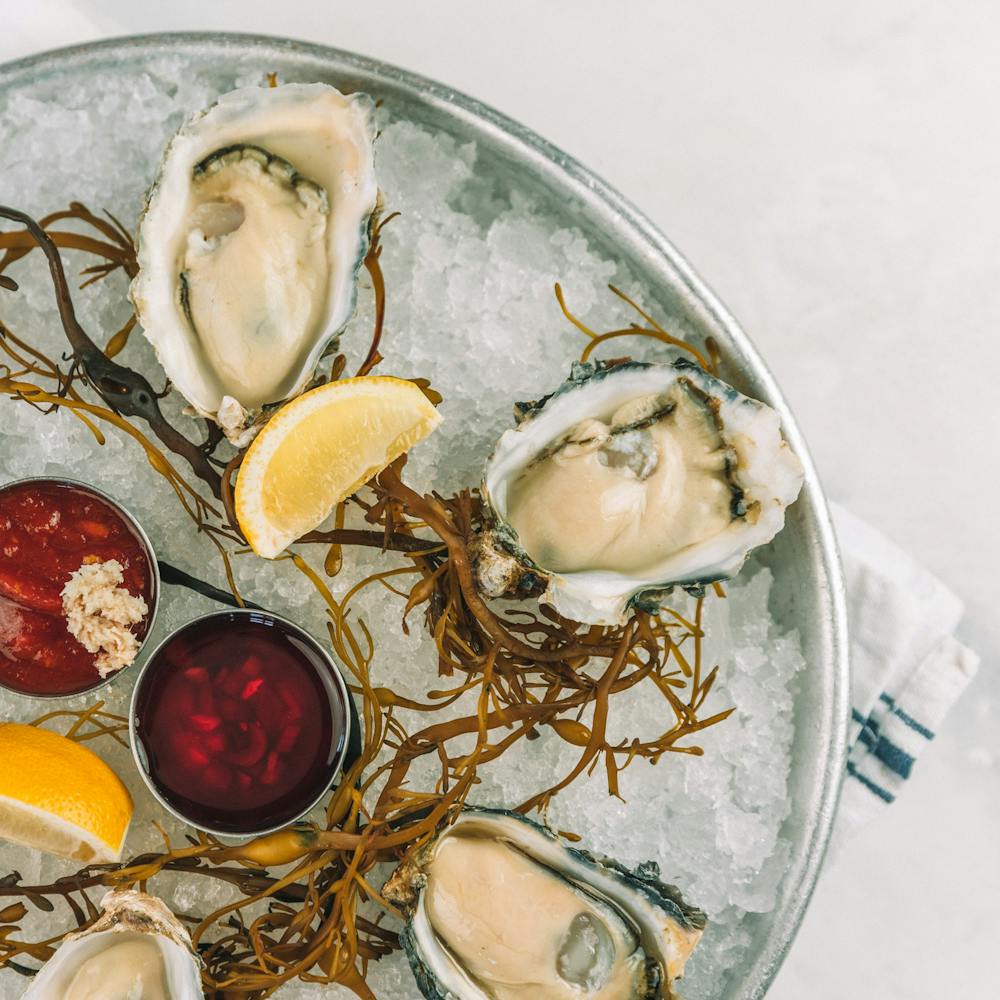 oysters on the half shell on a bed of ice with lemon and seaweed to garnish