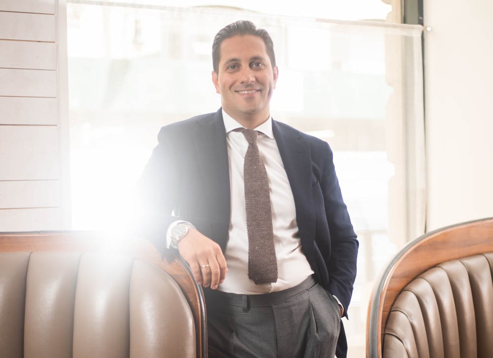 a man wearing a suit and tie smiling at the camera