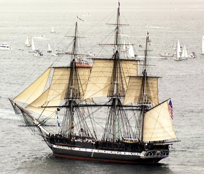 a large ship with sails with USS Constitution in the background