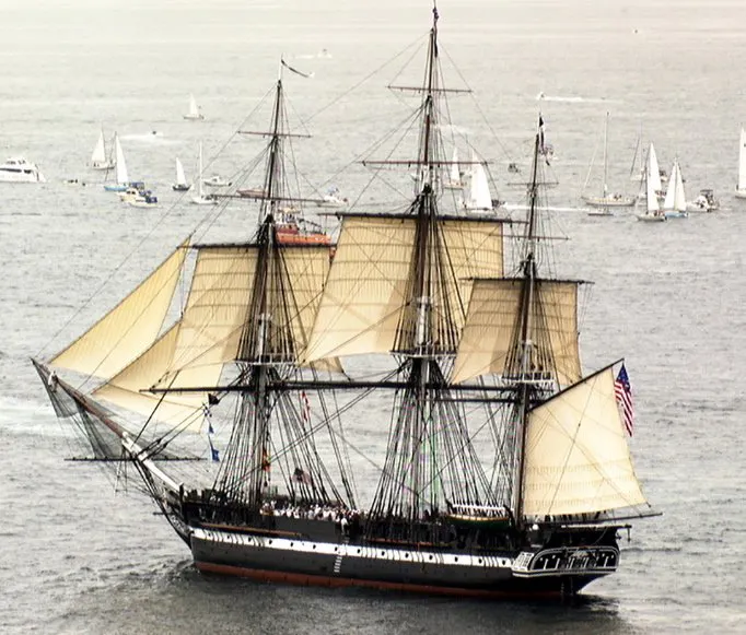 a large ship with sails with USS Constitution in the background