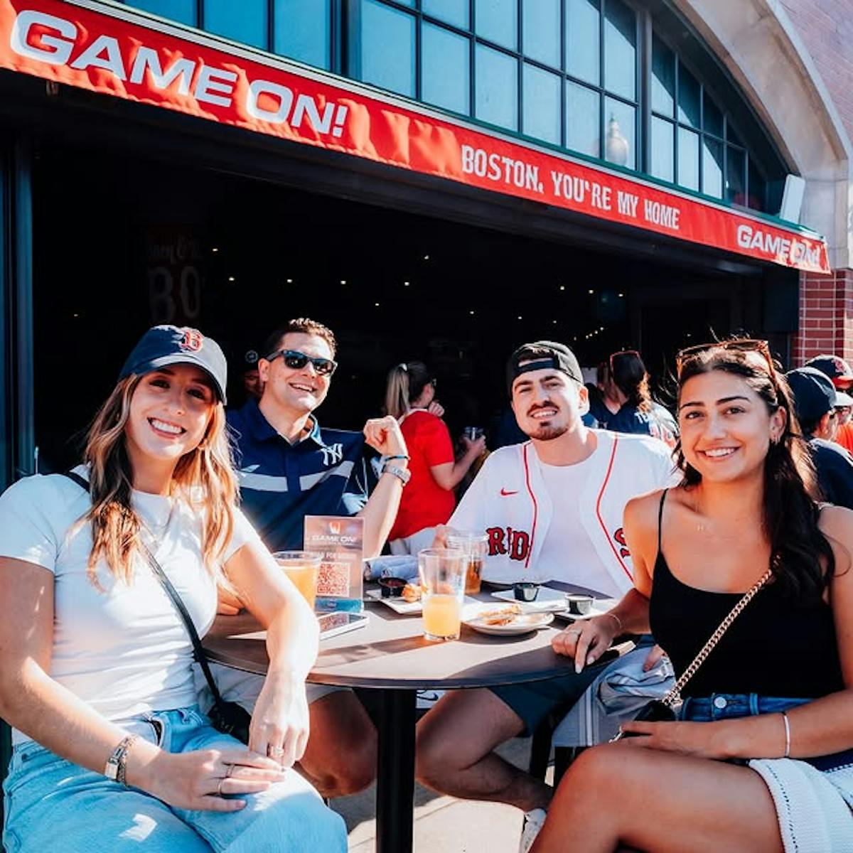 four people sitting outside on a patio wearing red sox merchandise
