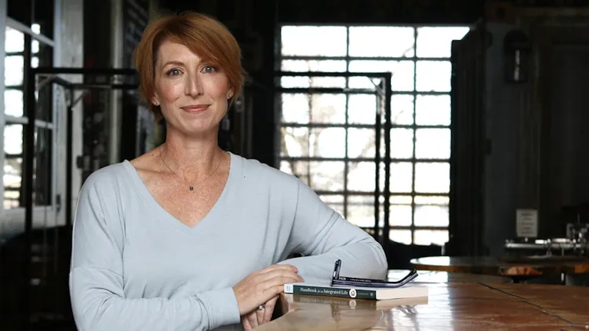 a woman sitting at a table with a laptop and smiling at the camera