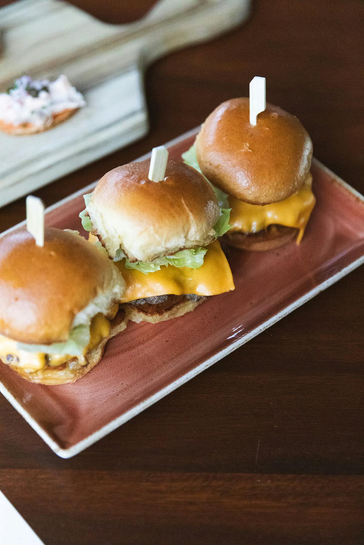 three cheeseburger sliders plated on a table at tesserae