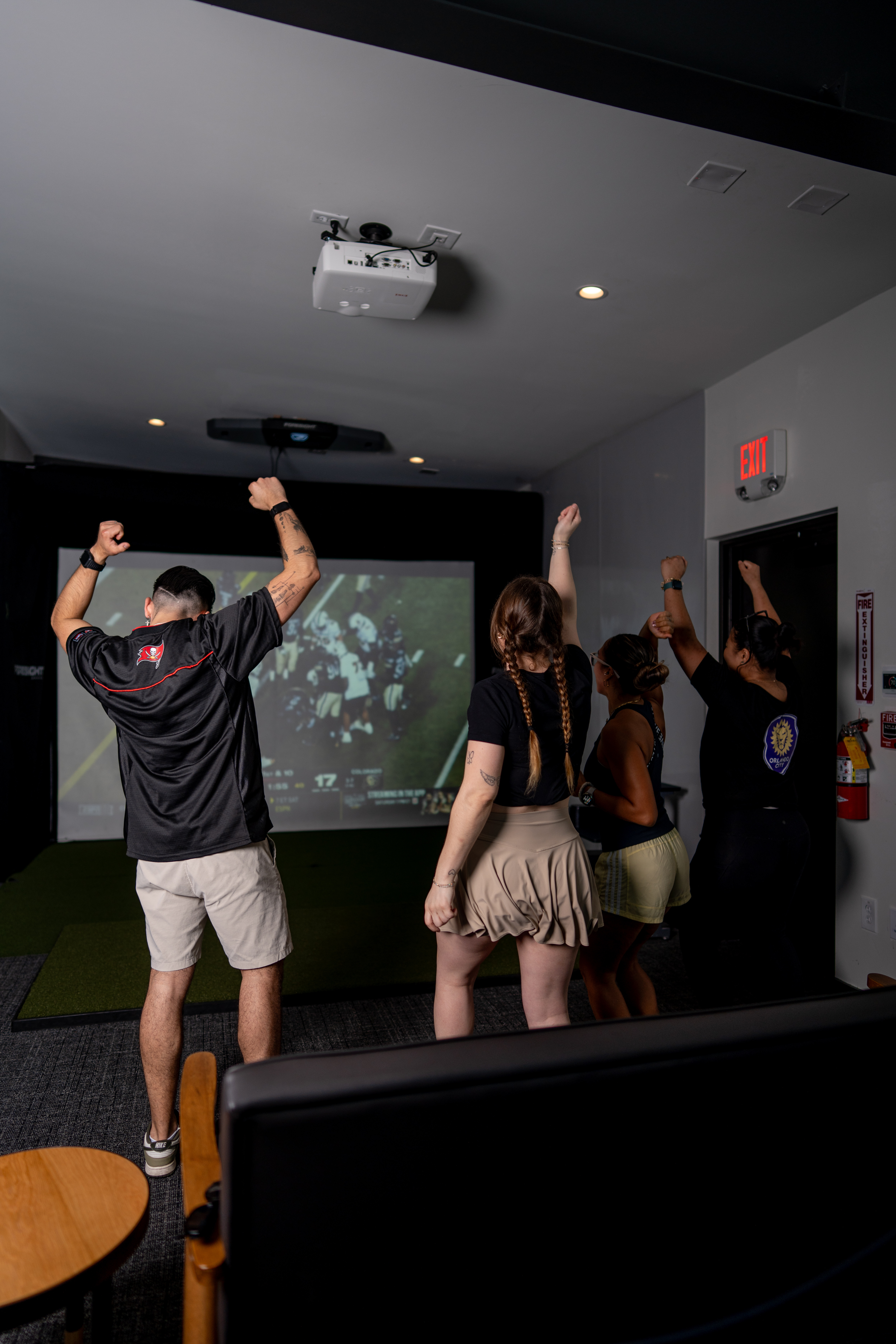 Group of friends cheering in the private game viewing room at 1983 in Tampa with the game on the projector screen
