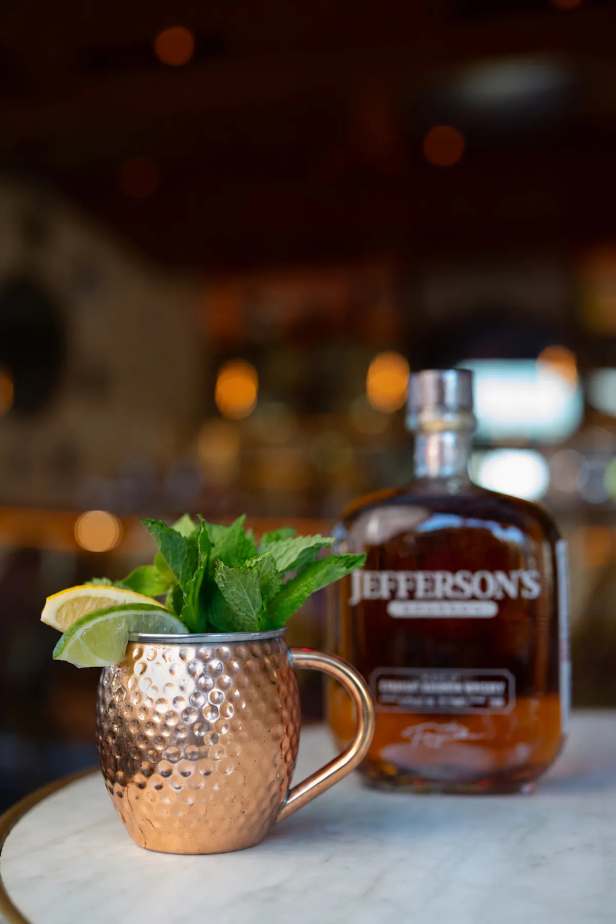 a copper mug with mint leaves and lime slices in it next to a bottle of liquor