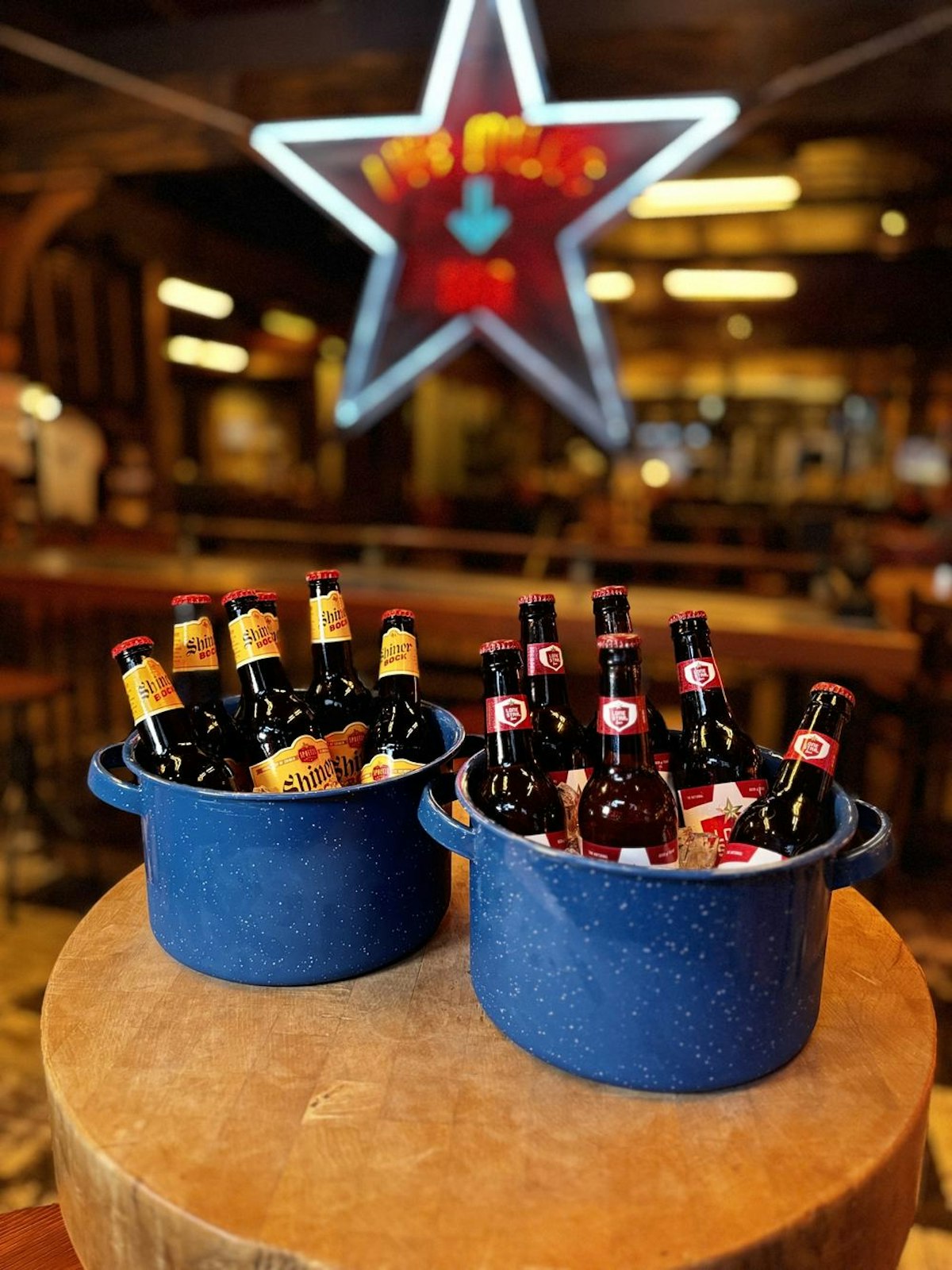 Two blue enamel buckets of iced beer bottles on a wooden barrel under a neon star