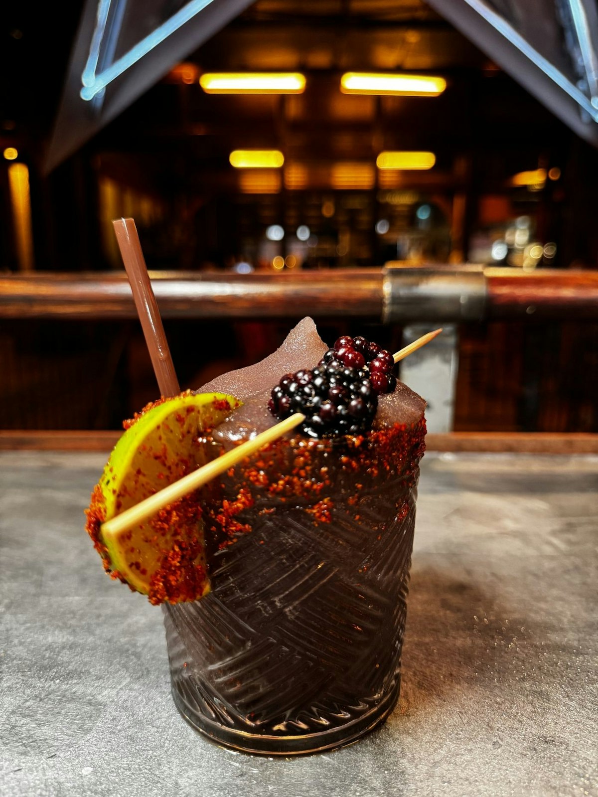 Frozen Blackberry Margarita with fresh blackberries and a lime wheel on the bar, neon star glowing behind it