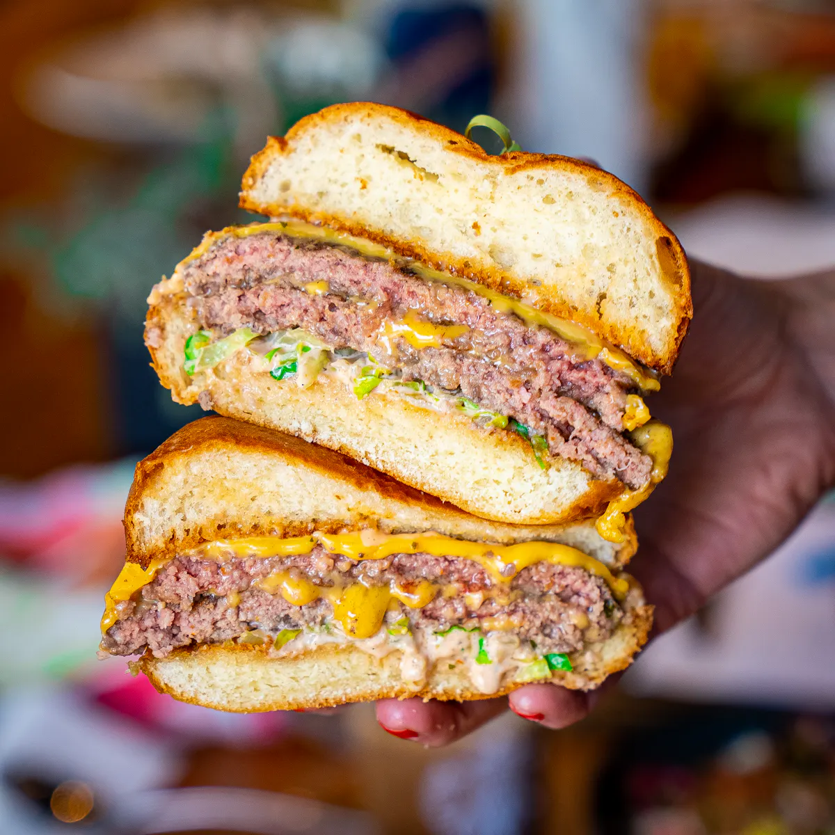 A close-up image of a hand holding a juicy burger with lettuce, tomato, and cheese visible between the buns