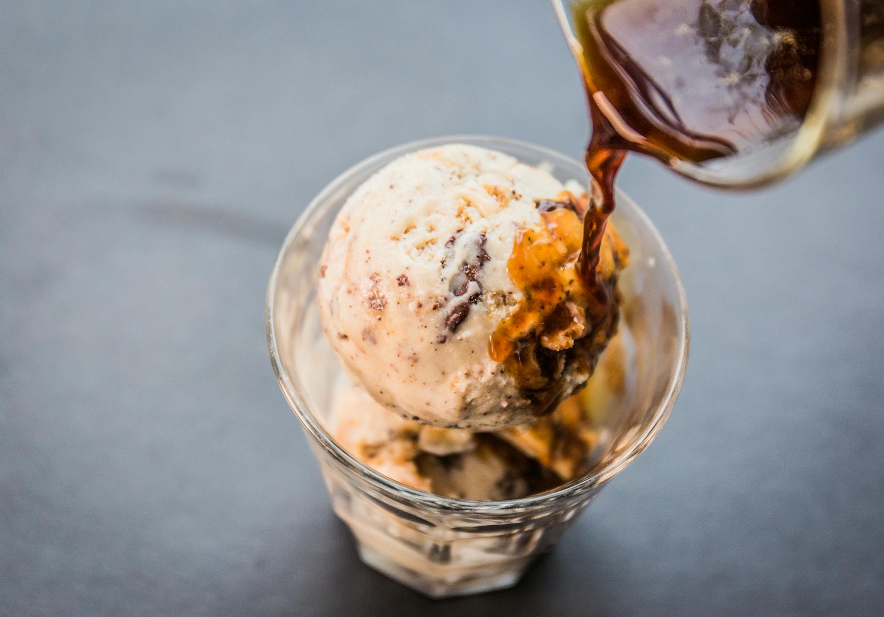 a glass pouring a dressing over a cup of ice cream