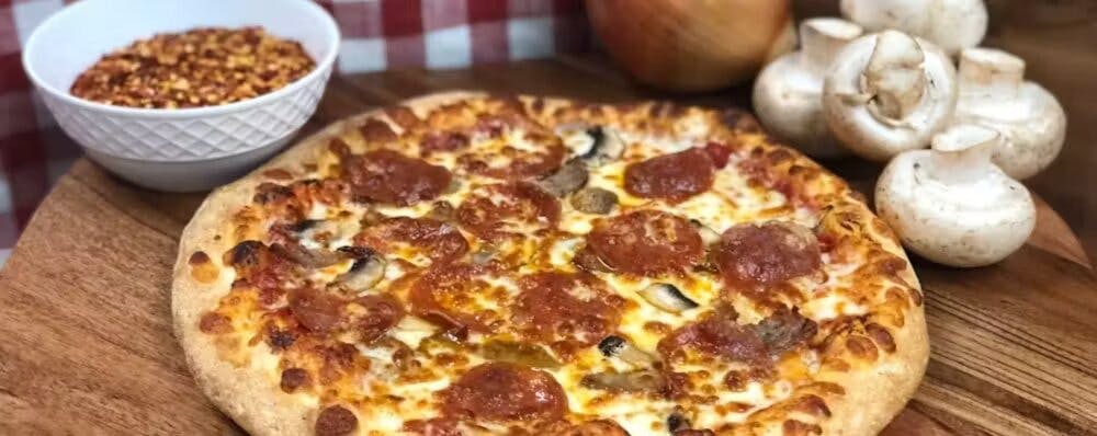 A mouthwatering, cheesy pizza with pepperoni and mushrooms A mouthwatering, cheesy pizza with pepperoni and mushrooms, placed on a wooden board with chilli flakes and mushrooms in either side towards the back.