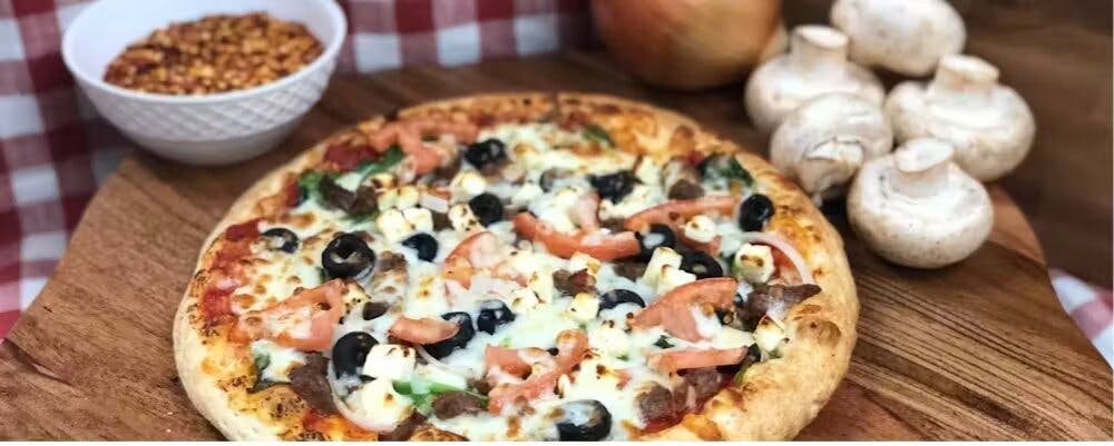 A delicious-looking pizza with a variety of toppings A delicious-looking pizza with a variety of toppings, on a wooden board with mushrooms and chilli flakes on either side of it in the back.