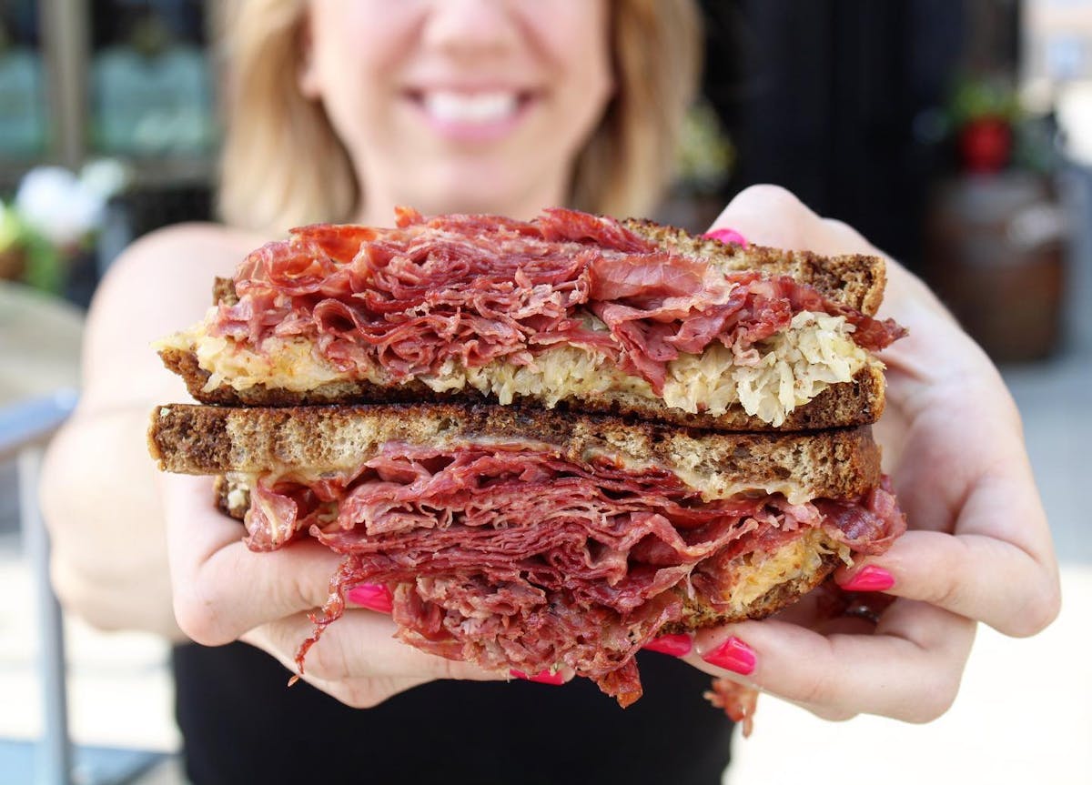 a close up of a woman holding a Reuben sandwich