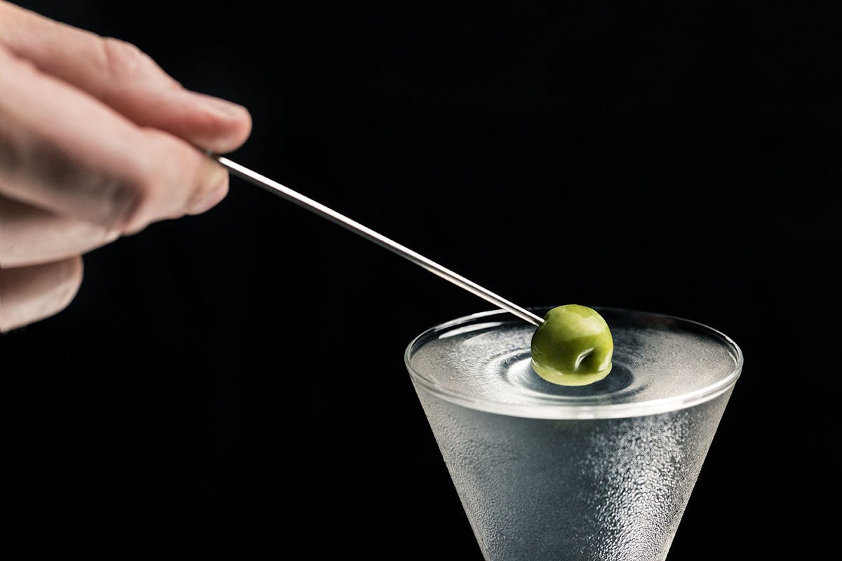 a hand holding an olive over a martini 