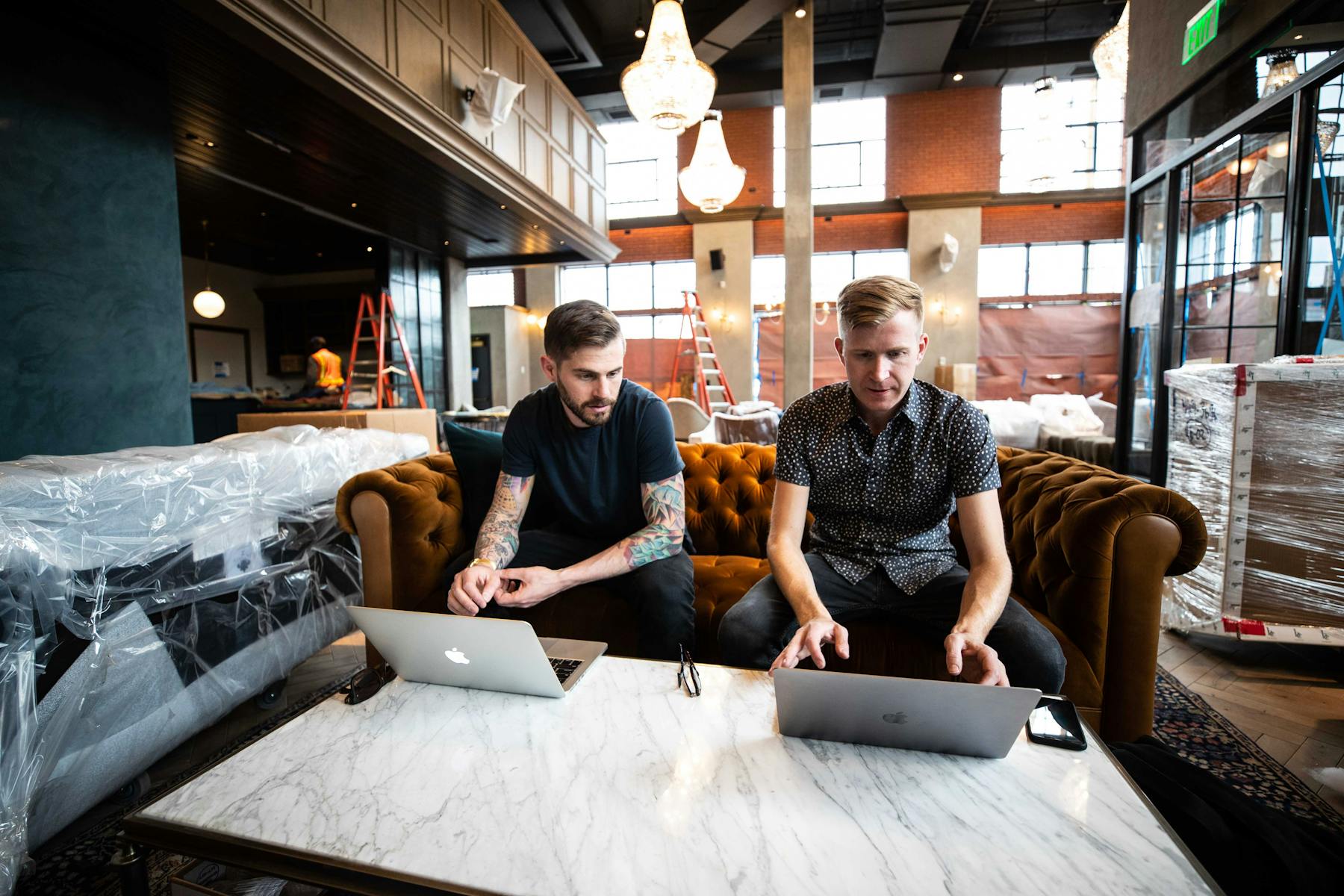 two men working on their Macs on a living room in their computer