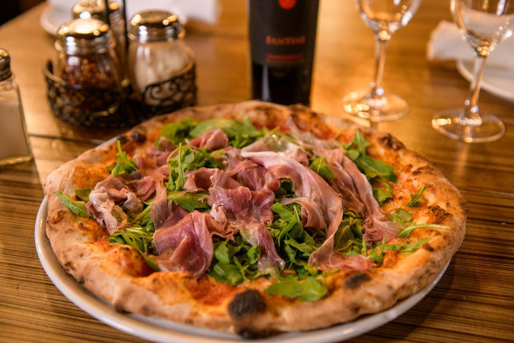 a pizza sitting on top of a wooden table topped with glasses of wine