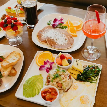 An image of Kimchi Fried Rice with a fried egg on a white plate with cocktails, pancakes, etc. on a table