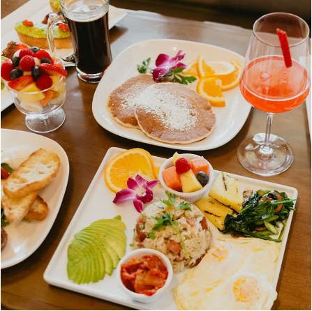 An image of Kimchi Fried Rice with a fried egg on a white plate with cocktails, pancakes, etc. on a table