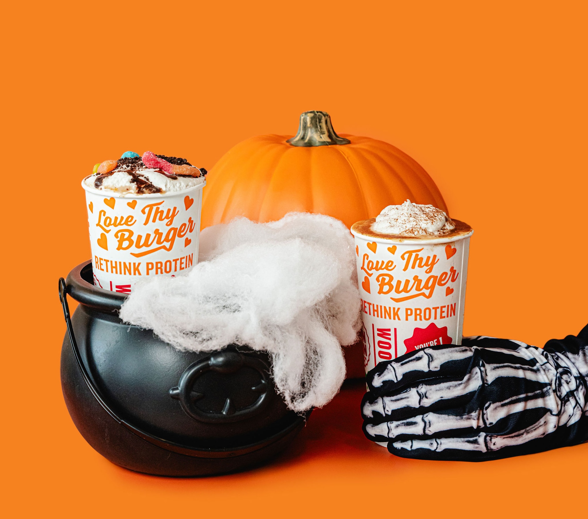 Halloween shakes with pumpkin and skeleton glove — one topped with gummy worms, the other with whipped cream and cinnamon.