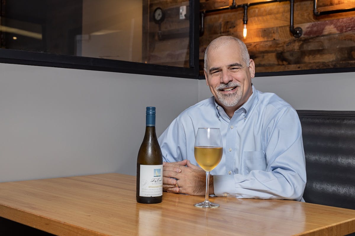 a man sitting at a table with wine glasses and smiling at the camera