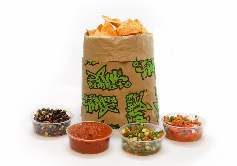 Chips on a brown paper bag and 4 different salsas
