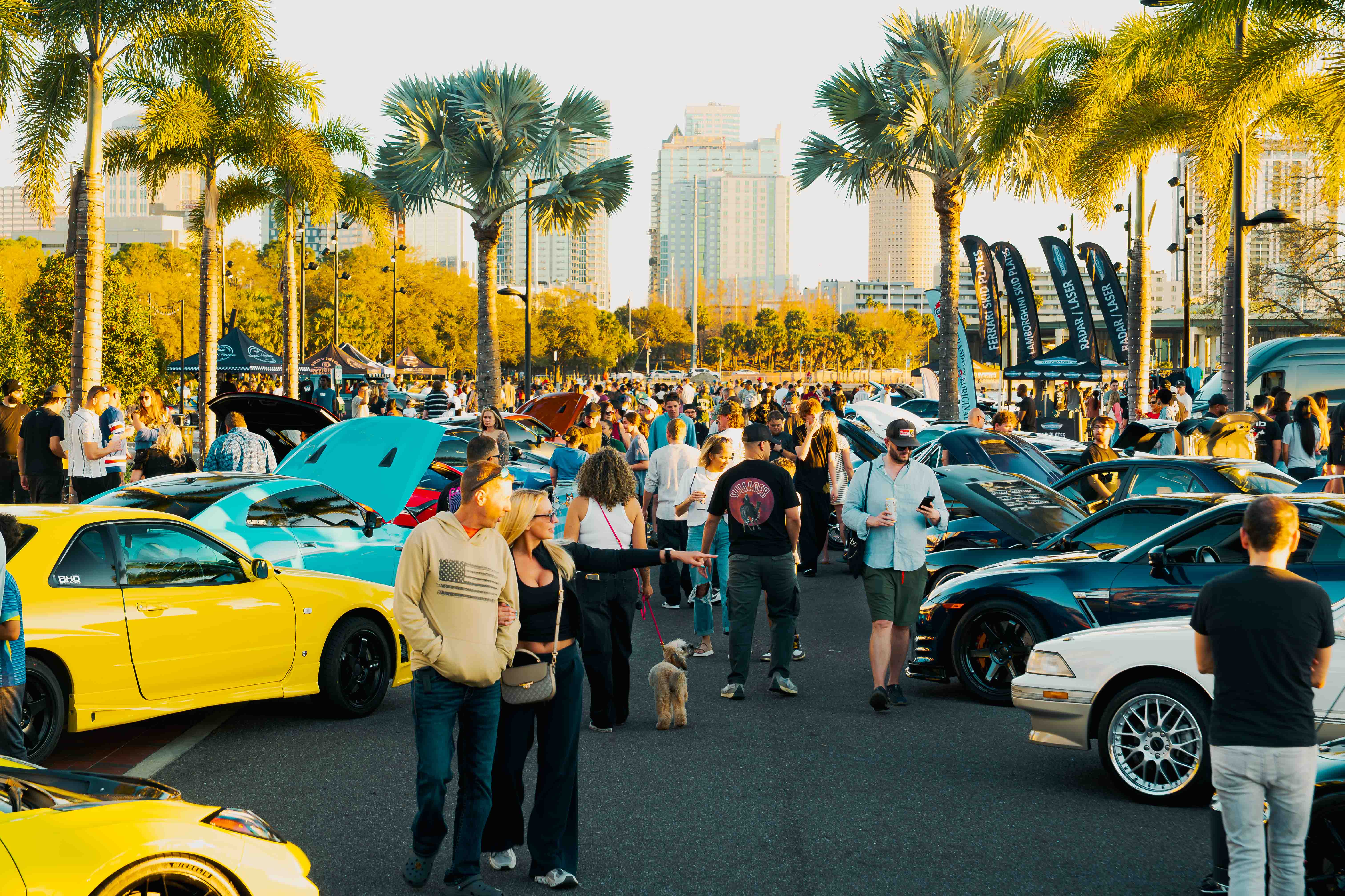 a group of people walking in a parking lot with cars and trees