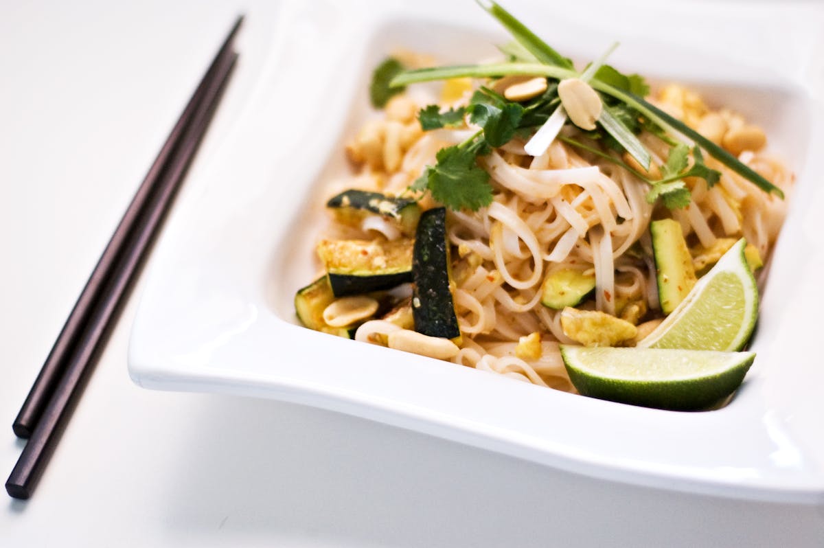 a bowl filled with thai noodles and shredded grilled chicken with vegetables