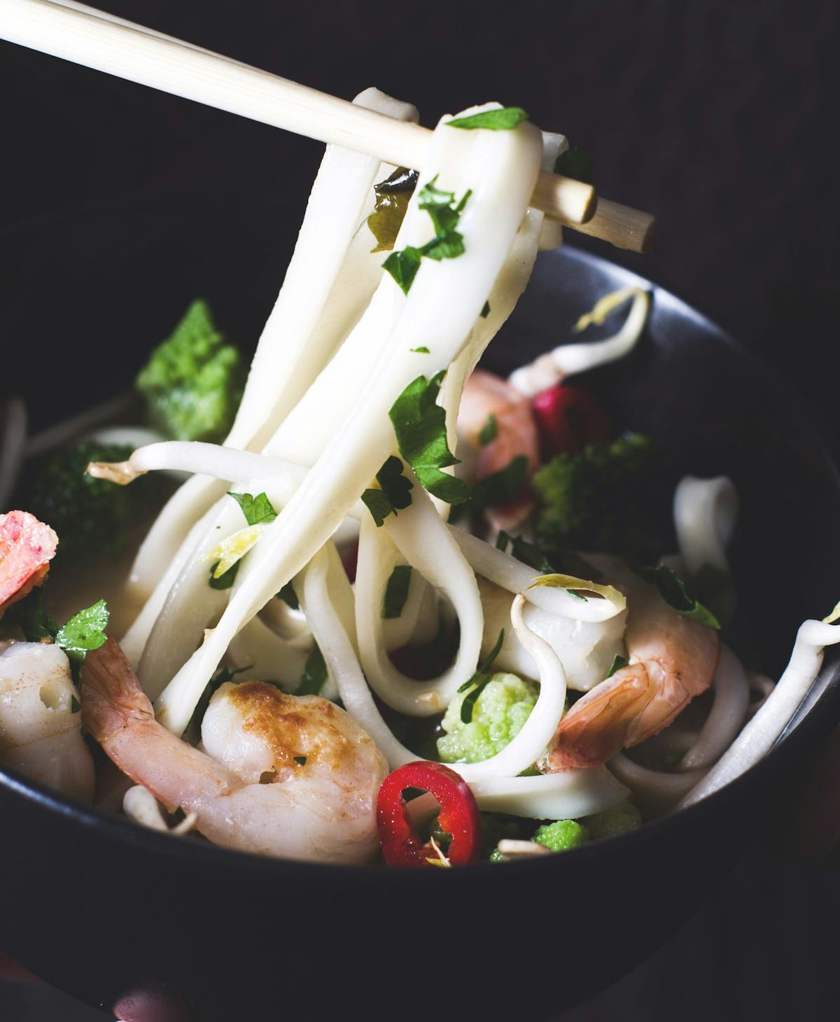 a bowl of white thai noodles with vegetables and meat