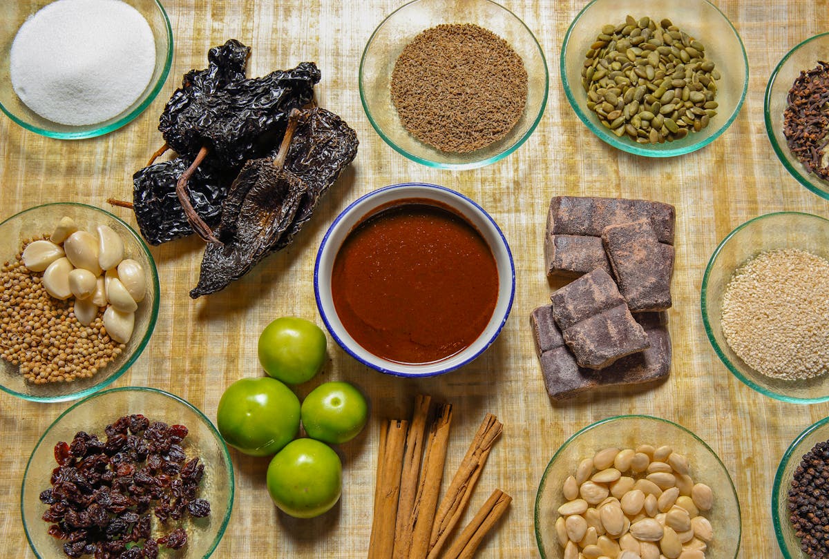 a variety of ingredients surrounding a brown sauce, including dried peppers, cinnamon sticks, and tomatillos.